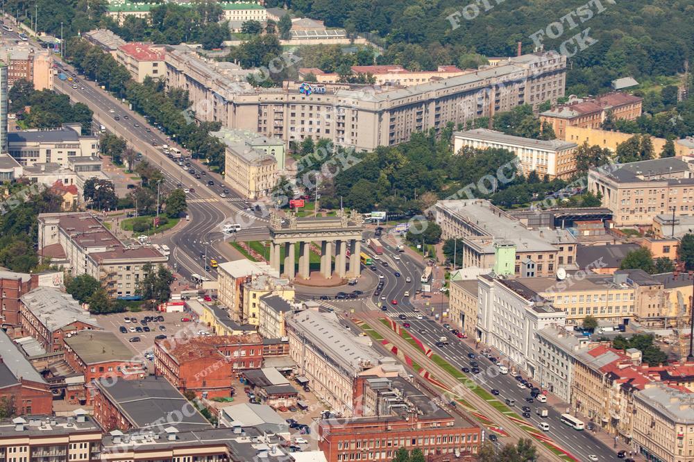 На фотографии изображена площадь Московских ворот в Санкт-Петербурге, снятая с высоты. В центре композиции находятся знаменитые Московские триумфальные ворота, возведённые в честь победы России в русско-турецких войнах. Этот район окружён историческими зданиями и оживлёнными улицами, по которым движутся автомобили. Вид с высоты позволяет оценить геометрию городской застройки и плотность городской среды в этой части Санкт-Петербурга.